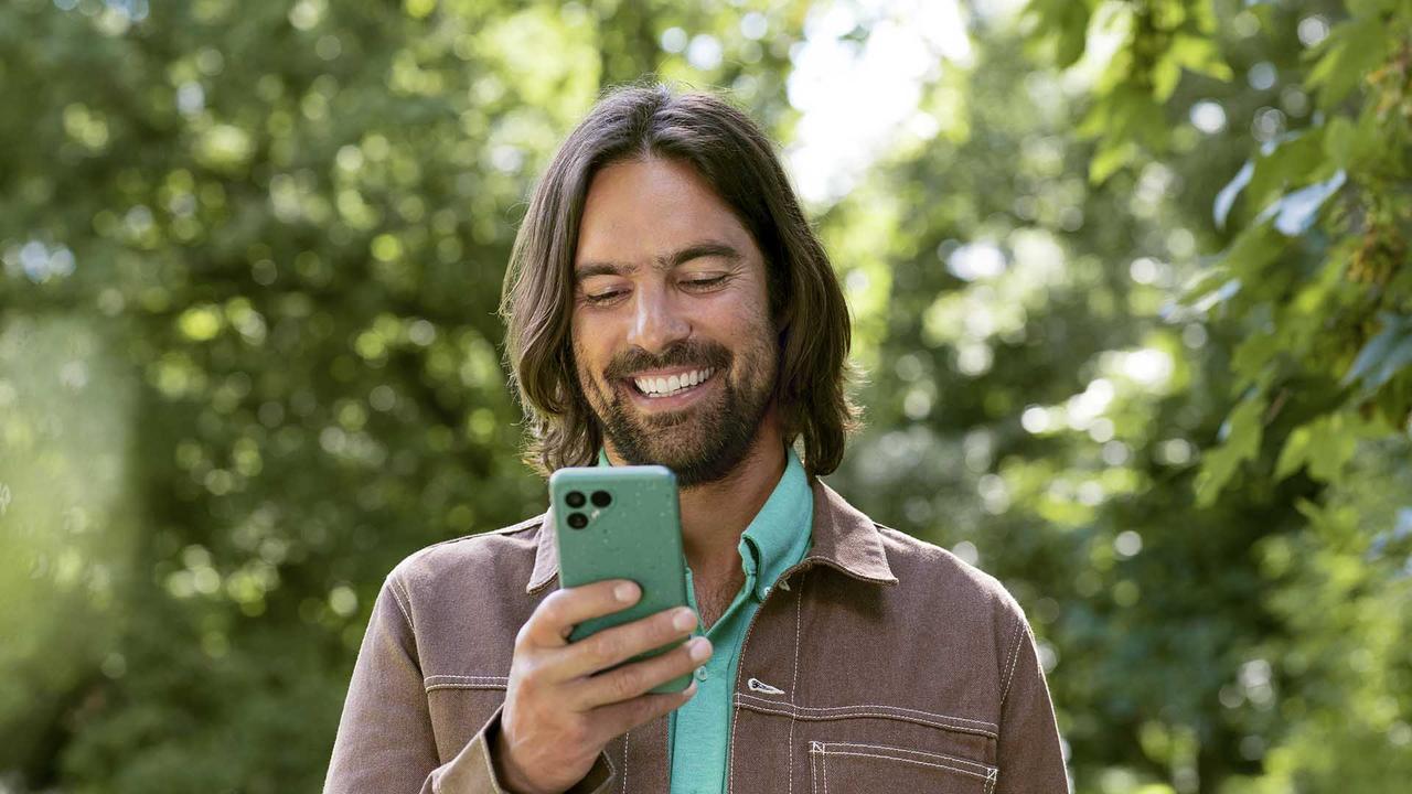 lächelnder Mann hält Fairphone 4 in sonniger Landschaft